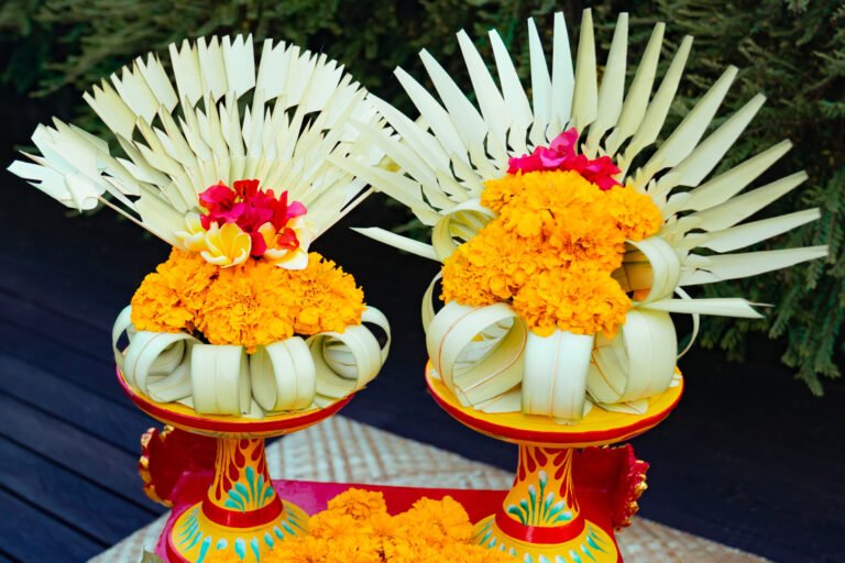 Two Balinese decorative ornaments made of palm leaves and yellow flowers on a ceremonial tray.